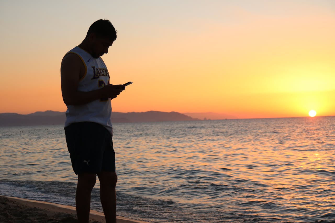 creative Man standing on the beach using a mobile phone during a serene sunset.